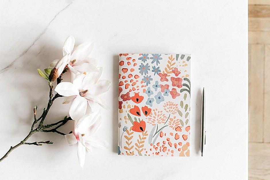 Notebook and pen beside flowers on a light desk